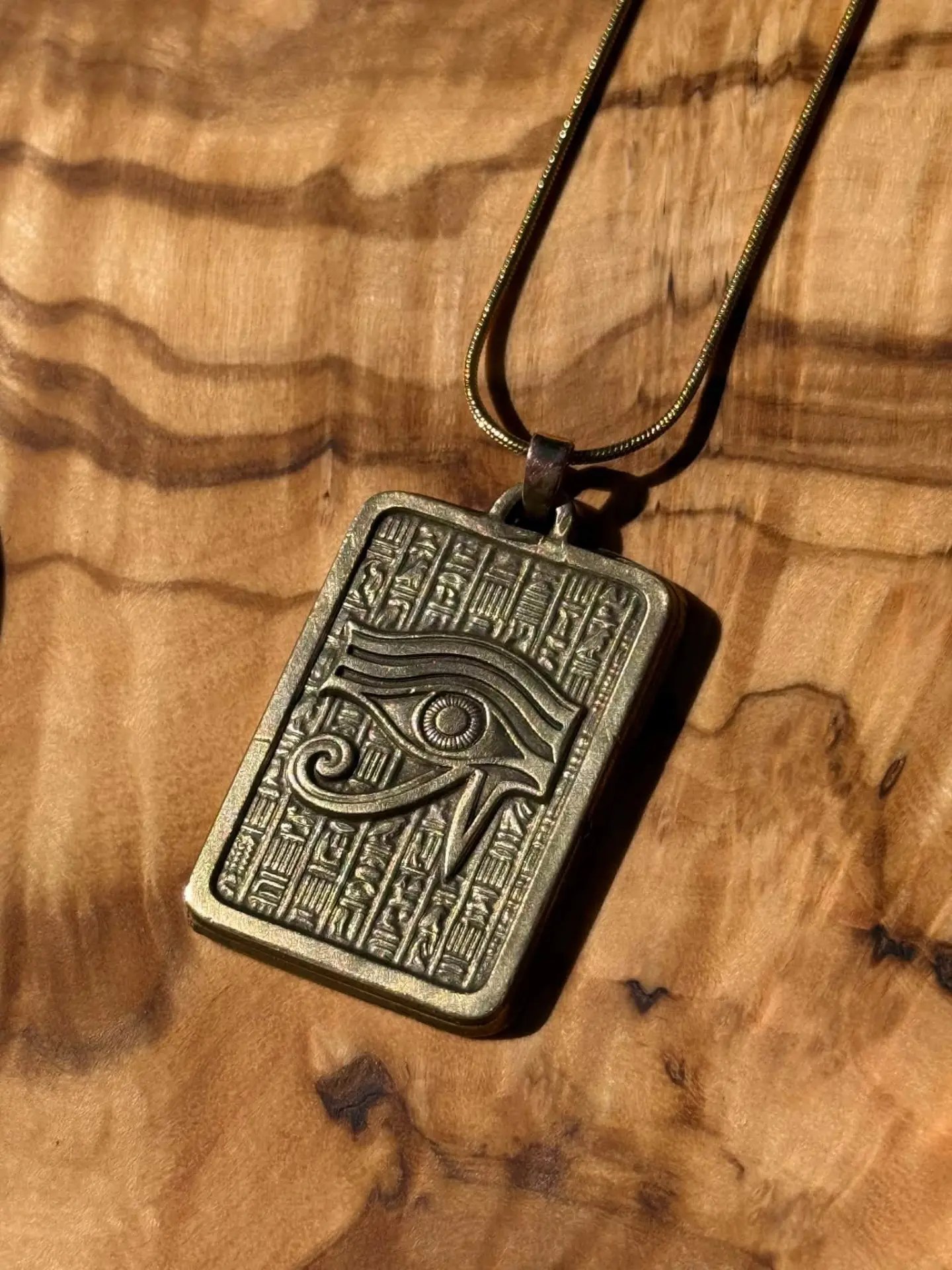 Engraved Eye of Horus pendant with hieroglyphic columns, resting on a wooden surface